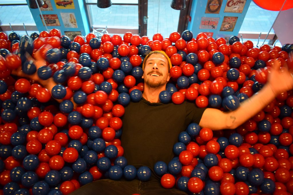 Kenny ligger i ett hav fullt av röda och blåa bollar.