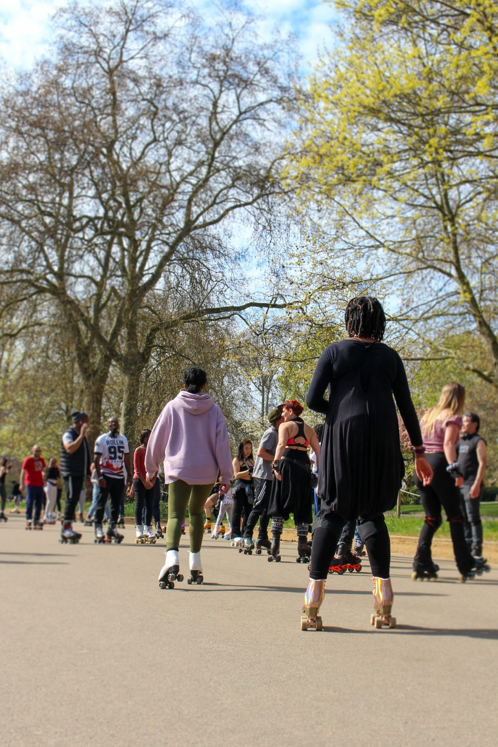 Ett tjugotal människor åker rullskridskor på asfalten i en park. I bakgrunden syns träd och gräs.