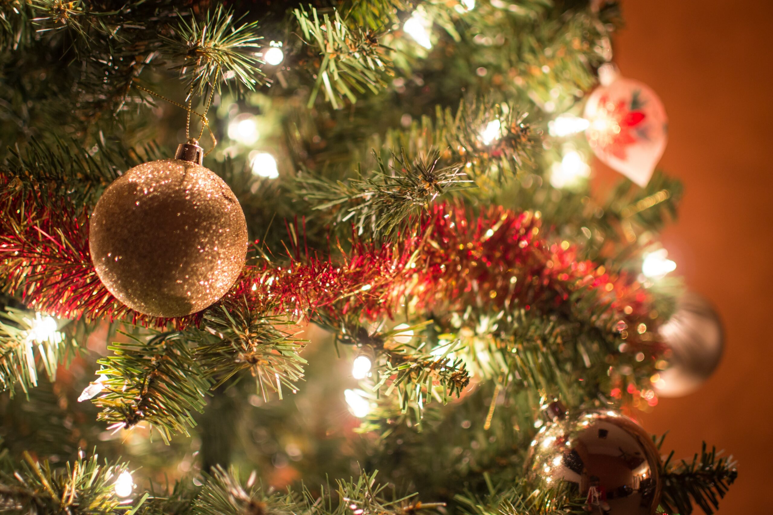 Närbild på en julgran som är pyntad med ljus, glitter och kulor.