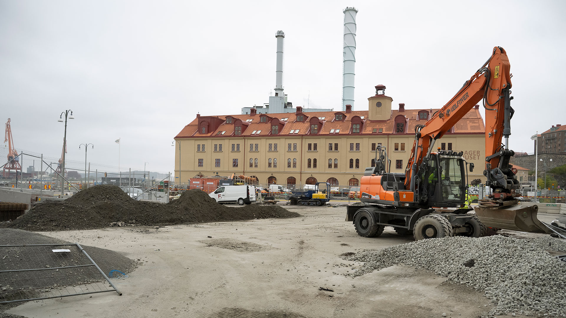 En byggarbetsplats med en grävmaskin. I bakgrunden syns Lagerhuset.
